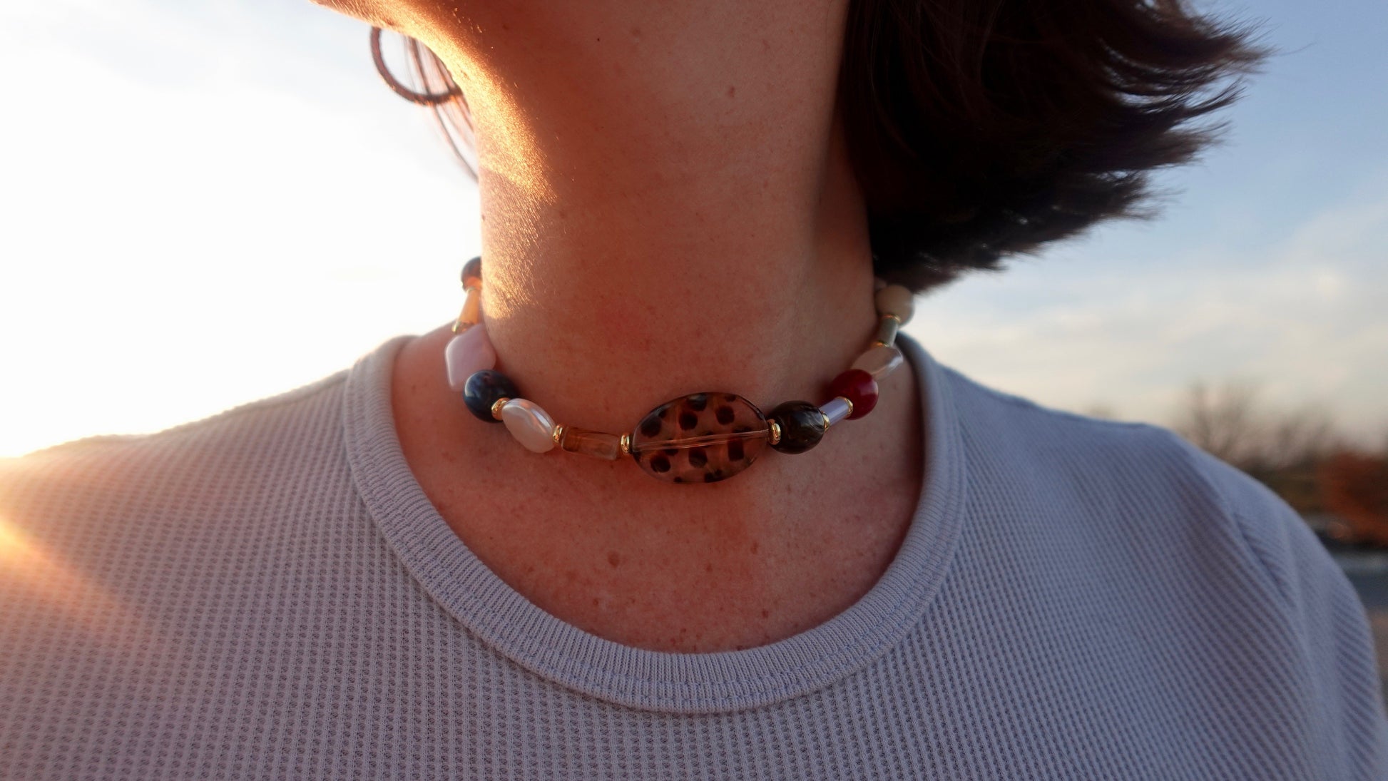 Person wearing a beaded necklace with a blurred outdoor background